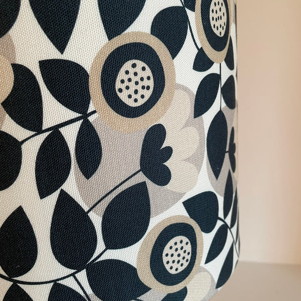 Handcrafted lampshade in graphic bloom fabric with repeating pattern of stylized flowers and leaves set against an off white background, close up, unlit.