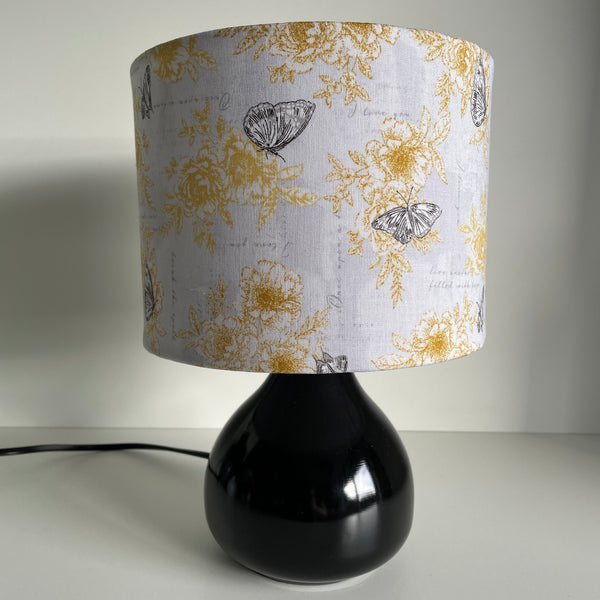 Small drum lampshade in summer romance fabric on small black lamp base, unlit, sold by shades at grays