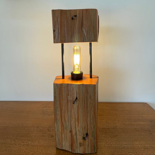 Wood table lamp made by shades at grays from 2 solid blocks of tōtara wood and metal tubes, front view, lit.
