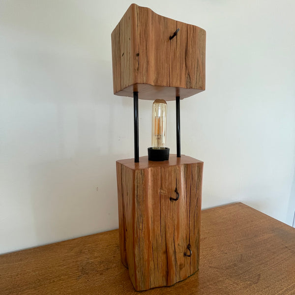 Wood table lamp made by shades at grays from 2 solid blocks of tōtara wood and metal tubes, front view, unlit.