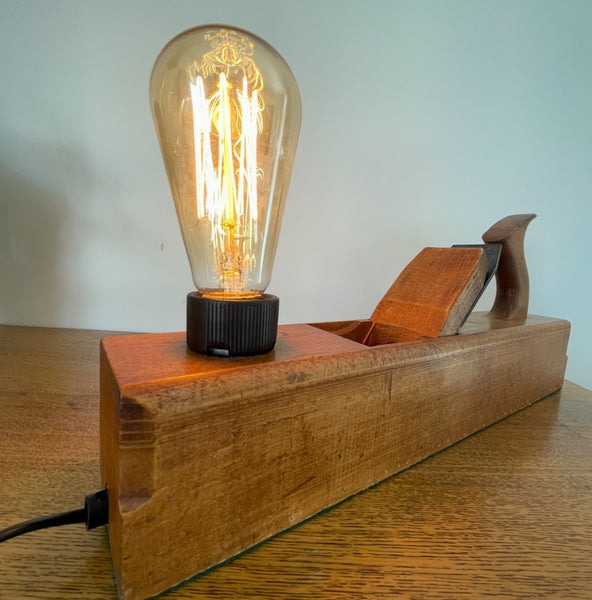 Wood table lamp upcycled by shades at grays from authentic carpenters plane with replica edison bulb, lit, front view and black lead.