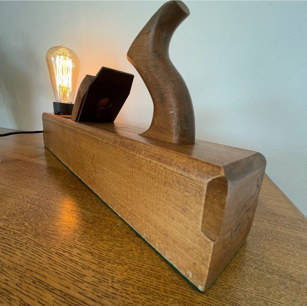 Wood table lamp upcycled by shades at grays from authentic carpenters plane with replica edison bulb, lit, side and front edge view.
