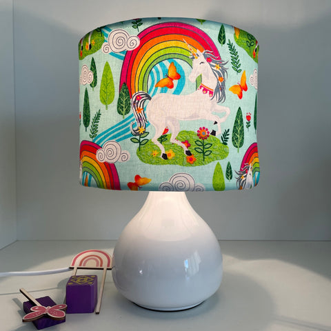 Small drum fabric lamp shade with white unicorn and orange butterflies, on white base, lit.