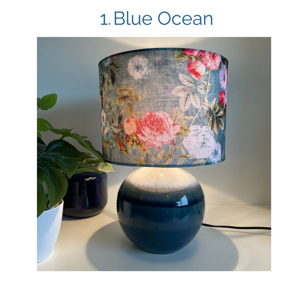 Blue ocean fabric lampshade on blue ceramic base, lit, by shades at grays.