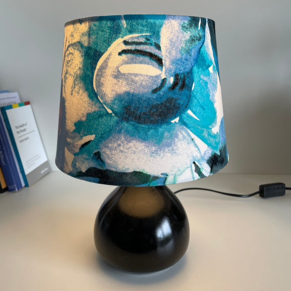 21 cm tapered lampshade, handcrafted in watercolour fabric on black base, lit.