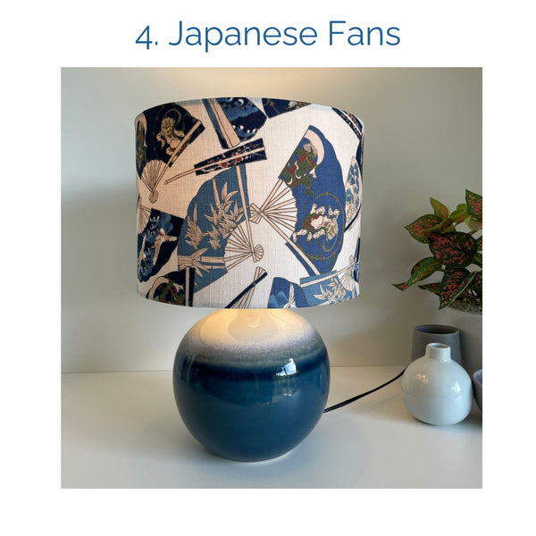 Japanese fans fabric lampshade on blue ceramic base, lit, by shades at grays.