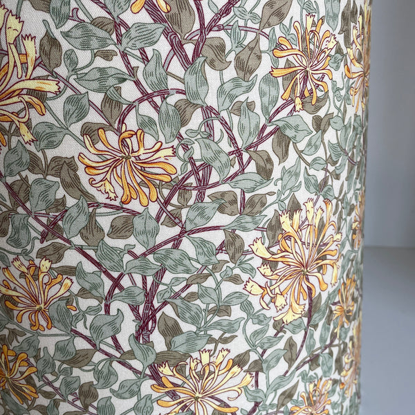A close-up of lampshade featuring a botanical pattern of yellow-orange flowers and muted green leaves on a white background.