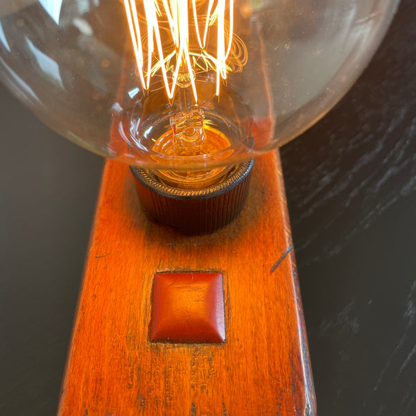 Vintage carpenter's wood plane table lamp crafted by shades at grays, close up of lit bulb and top grain..
