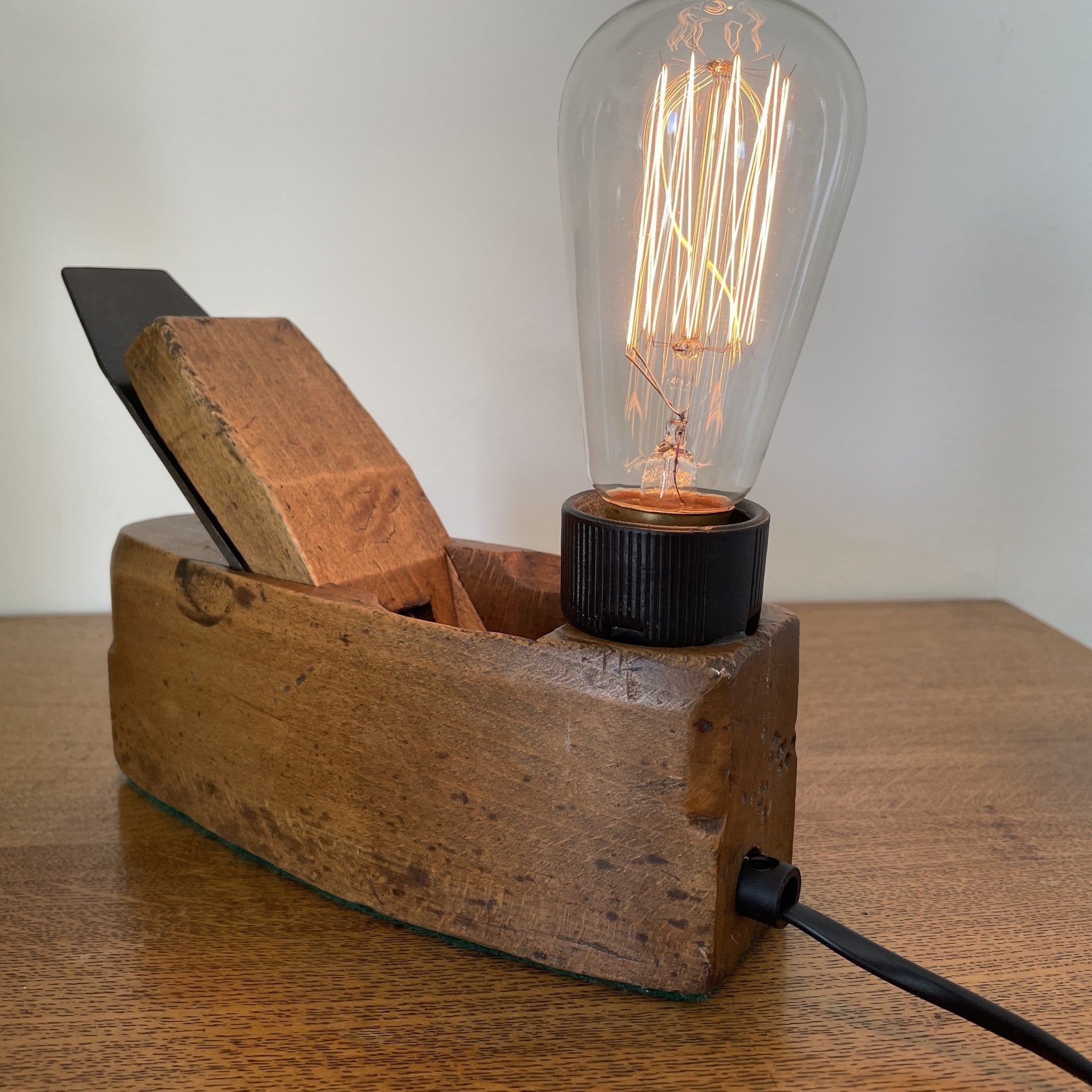 Authentic carpenters' plane upcycled into wood table lamp with edison bulb, lit, crafted by shades at grays, side view and back with black lead.