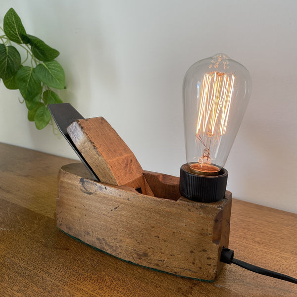 Authentic carpenters' plane upcycled into wood table lamp with edison bulb, lit, crafted by shades at grays, side view and back with black lead and long view of the cutting blade.