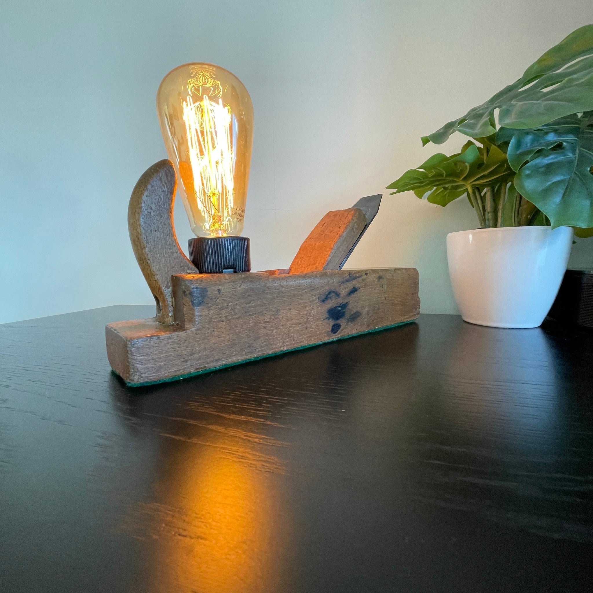 Authentic carpenters plane upcycled by shades at grays into wood lamp with edison lamp, lit, long front view.