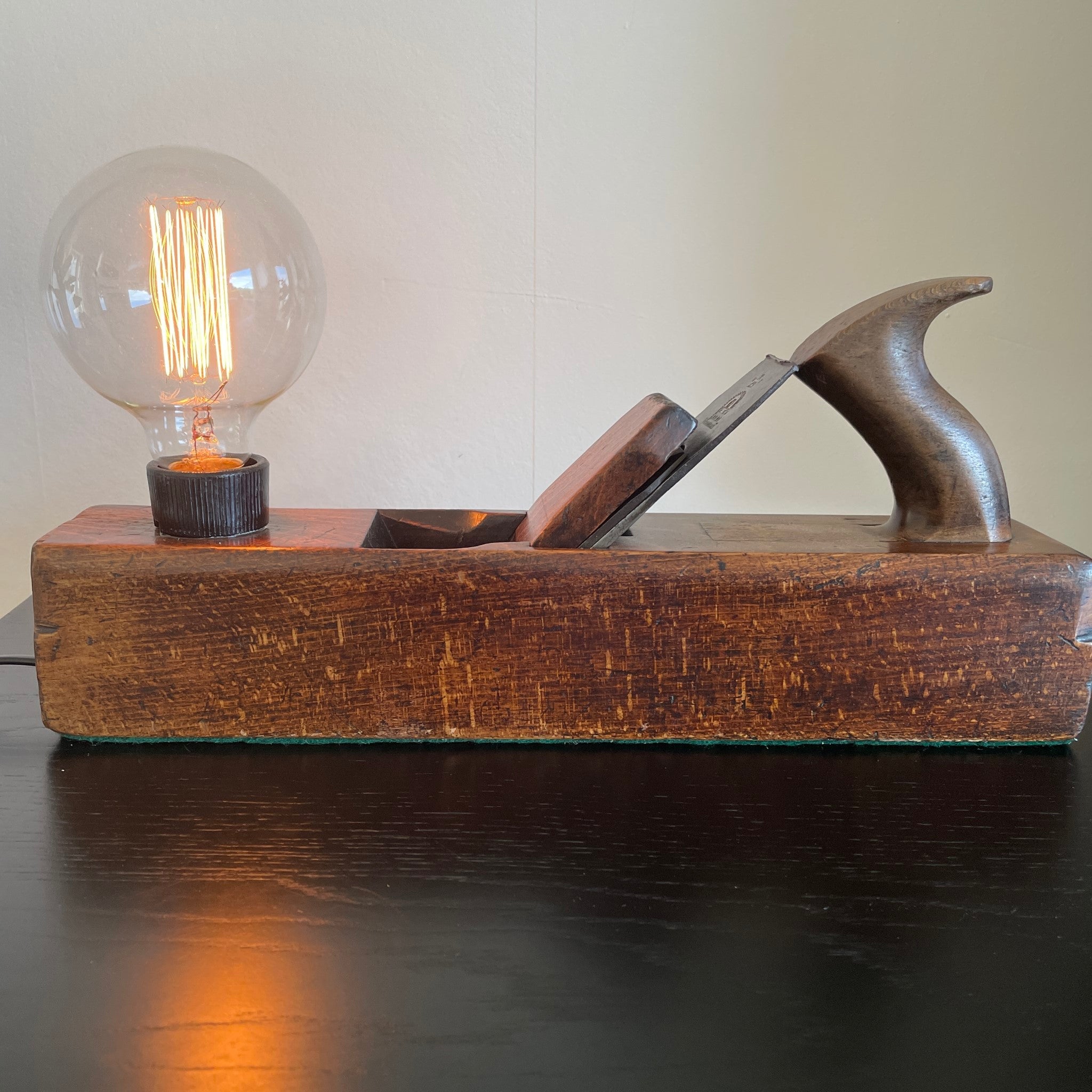 Authentic carpenters plane upcycled by shades at grays into unique lamp with edison bulb, lit. Front view.