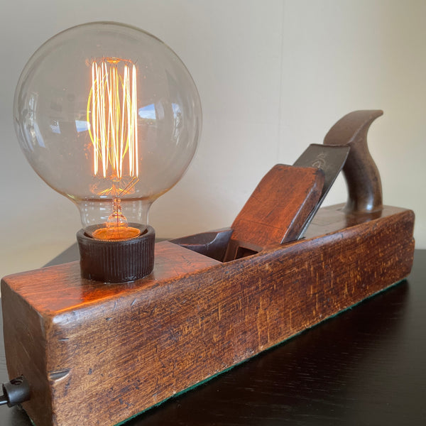 Authentic carpenters plane upcycled by shades at grays into unique lamp with edison bulb, lit, Close up of diagonal view.