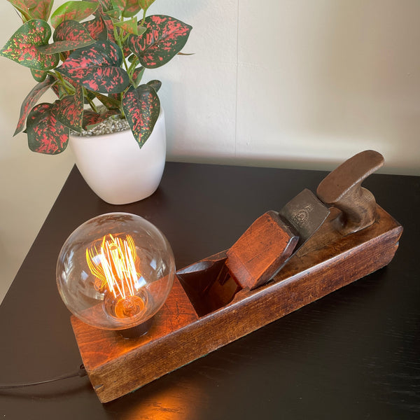 Authentic carpenters plane upcycled by shades at grays into unique lamp with edison bulb, lit, top view.