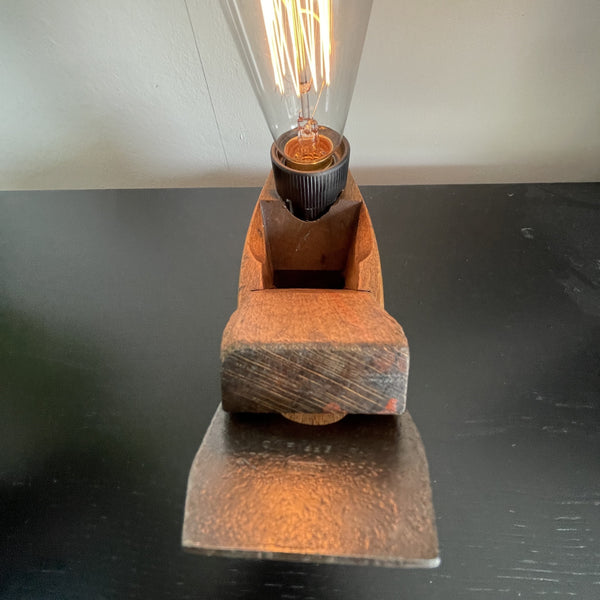 Authentic carpenters plane upcycled to wood table lamp with edison bulb, lit, crafted by shades at grays, close up of blade detail.