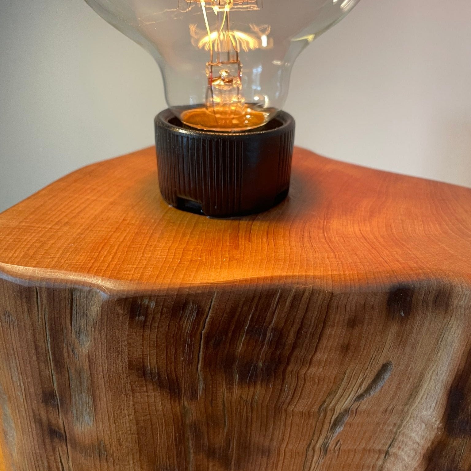 Smooth top and tabby markings on one smooth side of tōtara wood table lamp, with replica edision bulb, lit, close up, handcrafted by shades at grays.