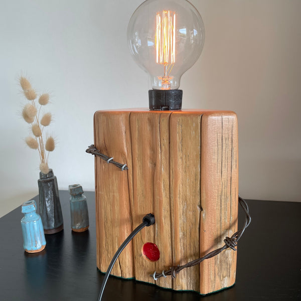 Authentic tōtara fence post upcycled by shades at grays to unique lamp with edison bulb, lit, back view.