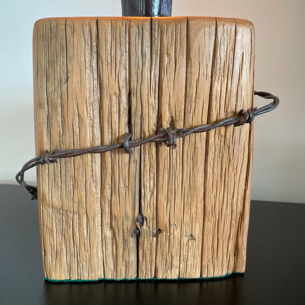 Authentic tōtara fence post upcycled by shades at grays to unique lamp with edison bulb, lit, close up of original barb wire.