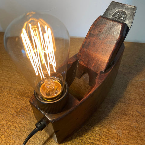 Wood table lamp crafted from authentic carpenters plane, dating back 100 plus years, with replica edison bulb, lit, and original brand on cutting blade, sold by shades at grays.