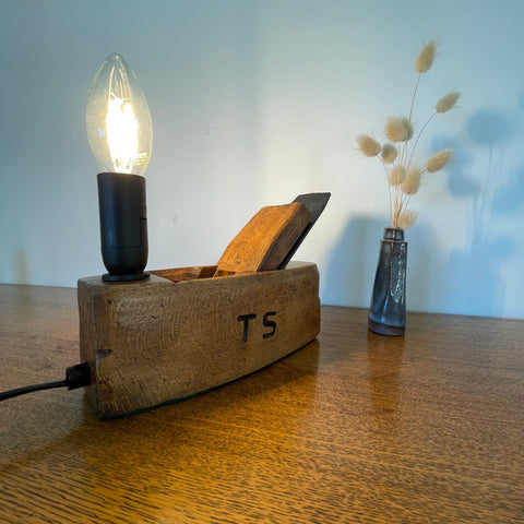 Authentic wood plane lamp with candle style bulb, lit, upcycled by shades at grays, front view with carpenters initials.