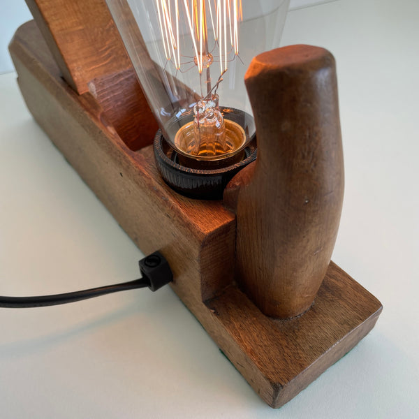 Back view of wooden table lamp crafted from old carpenter's wood block plane, with edison bulb, black lead.