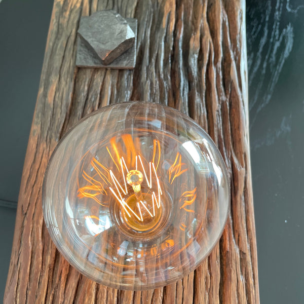 Wooden table lamp upcycled from wharf timber with addition of replica edison bulb, close up of lit bulb and original bolt.