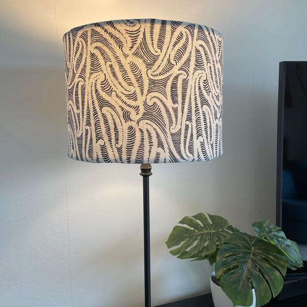 Bespoke medium sized drum lampshade by shades at grays, nz with Aho Creative fabric, on black stand, lit.