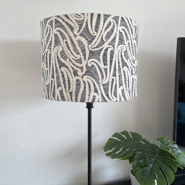 Bespoke medium sized drum lampshade by shades at grays, nz with Aho Creative fabric, on black stand, unlit.