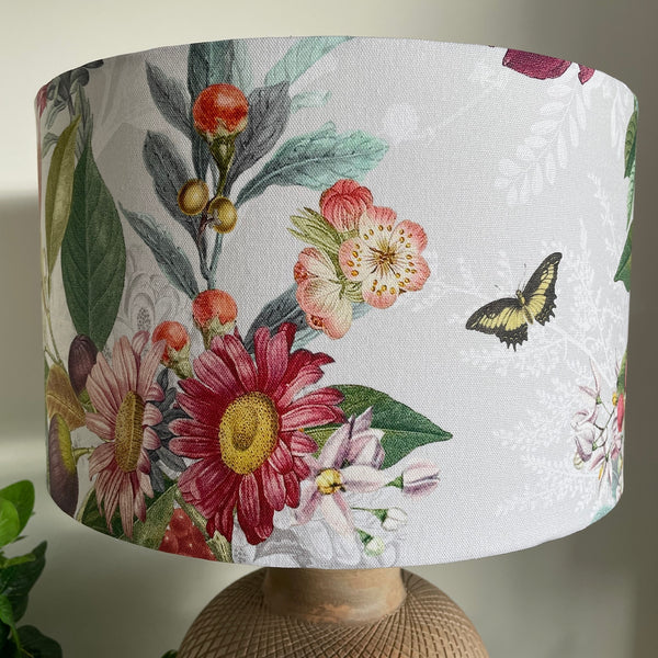 Butterfly and spring hedgerow flowers on a grey and white background, fabric lampshade unlit on terracotta base by shades at grays