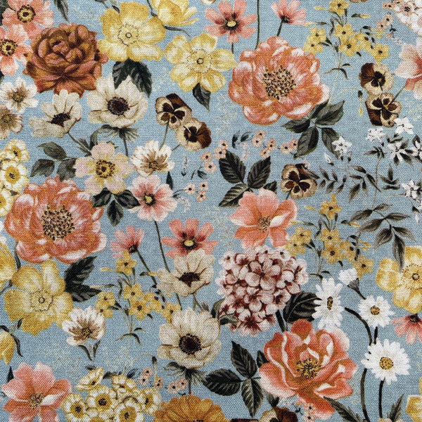 Close up of floral mix fabric with multicolour flowers in tones of browns and pinks and yellows with sage green foliage on a blue-grey background.