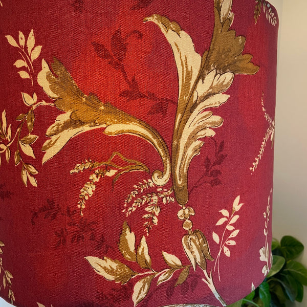 Close up of Large drum fabirc lamp shade made in nz by shades at grays, lit, gold foliage on red print.