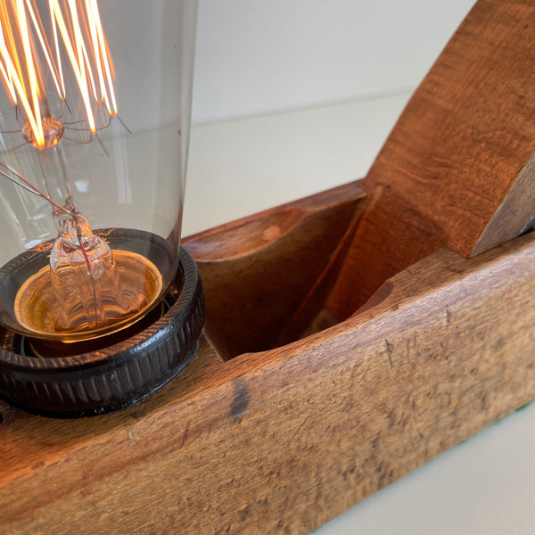 Close up of wooden table lamp crafted from old carpenter's wood block plane, with edison bulb, lit.