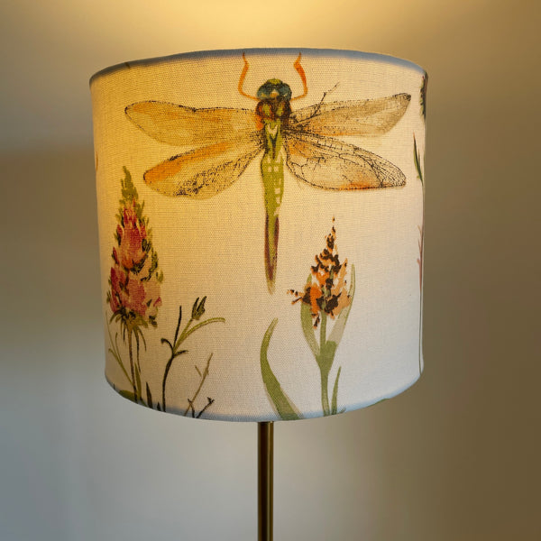 Cream dragonfly fabric on medium cylinder lampshade, lit.