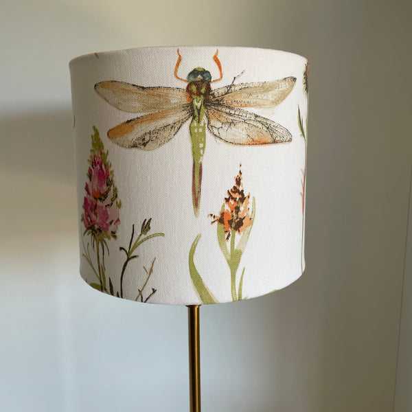 Cream dragonfly fabric on medium cylinder lampshade, unlit.