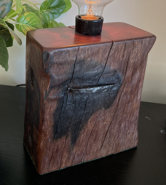 Deep red chocolate coloured wood table lamp with original marks, erosion and nail, top and front view, lit.