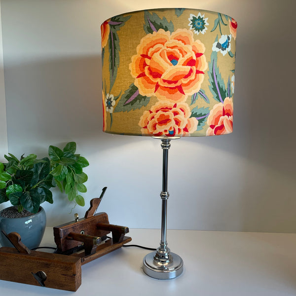 Drum style lampshade with Kaffe Fassett fabric, lit on brushed metal lamp base.