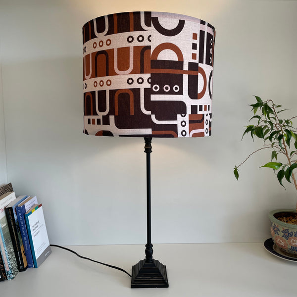 Large drum style lamp shade with geometric harmony tan, lit on black lamp base, by shades at grays, nz