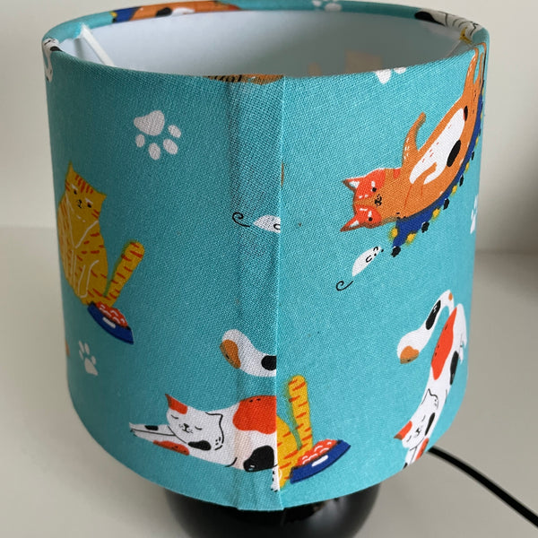 Lampshade  with a blue fabric shade featuring cat illustrations, close up of slightly flawed back seam.