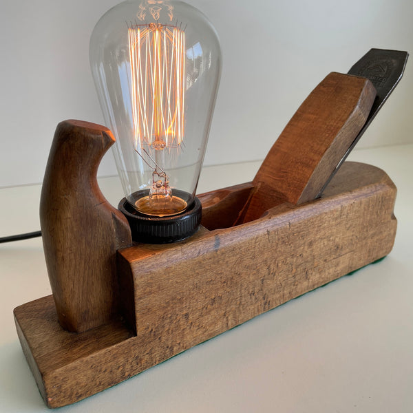 Front view and bismark handle of wooden table lamp upcycled from vintage carpenter's wood plane with edison bulb, lit.