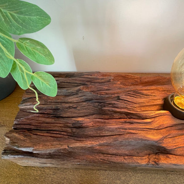 Handcrafted NZ lamp by shades at grays created from reclaimed timber, eroded contours, close up, top view, edison bulb, lit.