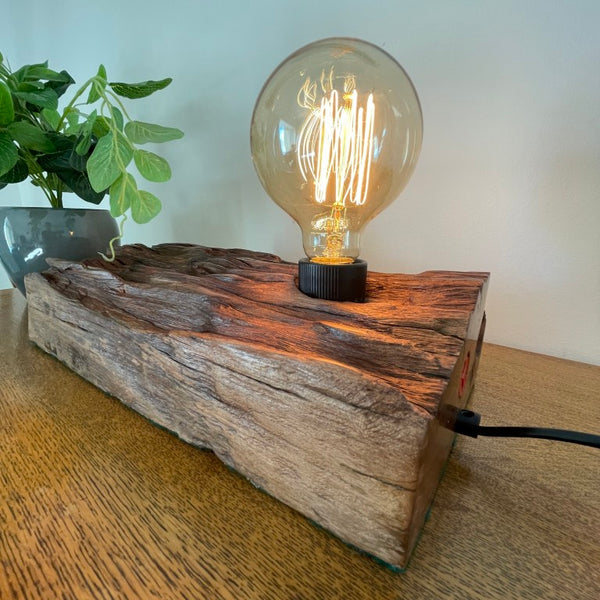 Handcrafted NZ lamp by shades at grays created from reclaimed timber, eroded contours, front and side view, edison bulb, lit.