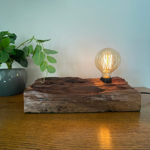 Handcrafted NZ lamp by shades at grays created from reclaimed timber, eroded contours, front view, edison bulb, lit.