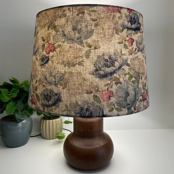 Handcrafted large tapered lampshade with blossoms on grey fabric, lit, on brown base by shades at grays.