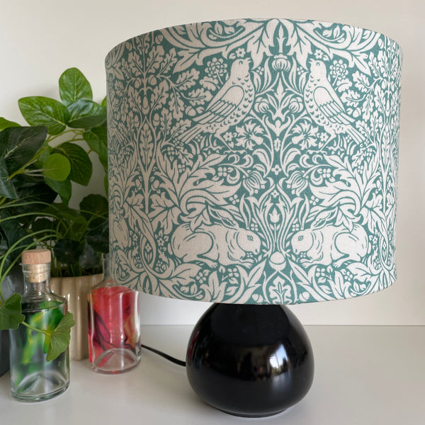 Handcrafted lampshade, medium drum with William Morris Brer Rabbitt fabric on small black lamp base, unlit, by shades at grays nz.