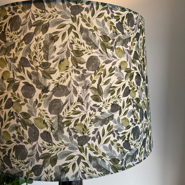 Handcrafted lampshade with Serenity Leaves fabric, close up by shades at grays, lit.