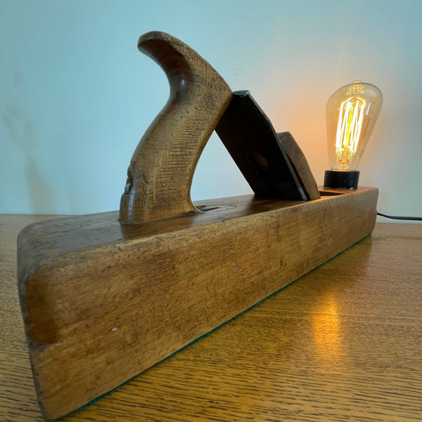 Heritage lamp crafted by shades at grays from original carpenters' half jack plane with replica edison bulb, lit, angled view.