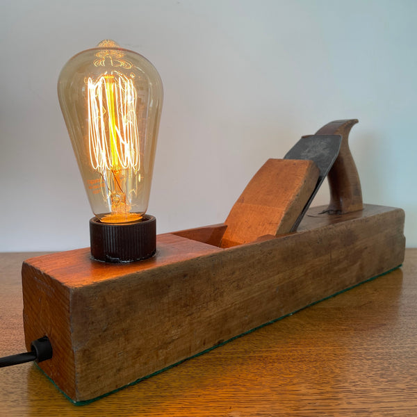 Heritage lamp crafted by shades at grays from original carpenters' half jack plane with replica edison bulb, lit, back and right side view.