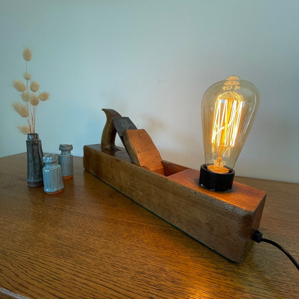 Heritage lamp crafted by shades at grays from original carpenters' half jack plane with replica edison bulb, lit, back and side view.