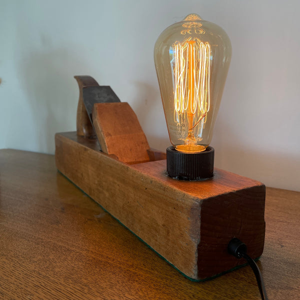 Heritage lamp crafted by shades at grays from original carpenters' half jack plane with replica edison bulb, lit, back  view.