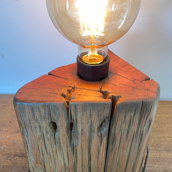 Heritage lamp upcycled from authentic totara post, close up of smooth top grain and replica edison bulb, lit.